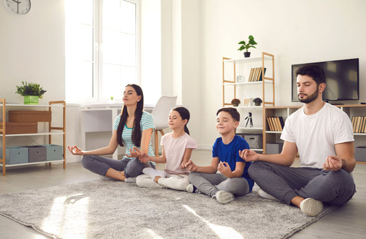 a family sitting down on the carpet at home in a Buddha position, closing their eyes and breathing the clean air from their home. They use Orana Essential to clean the air they breathe.