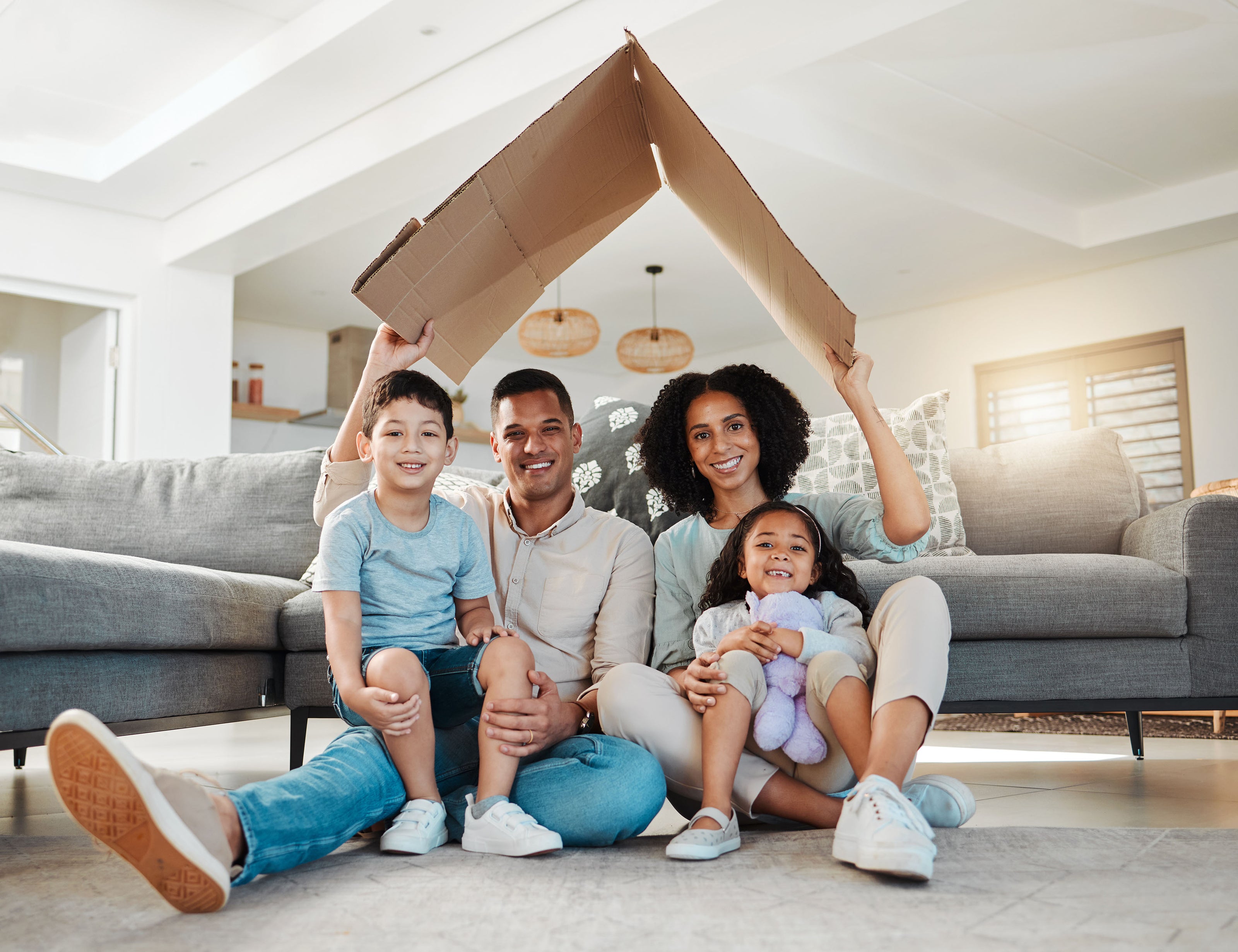 a picture of a happy multicultural family, 2 parents and 2 kids in their living room. They are sitting on the carpet and holding a cardboard as a roof. It is to signify that they feel safe and home being together. Our products are safe for kids, pets and also food safe.